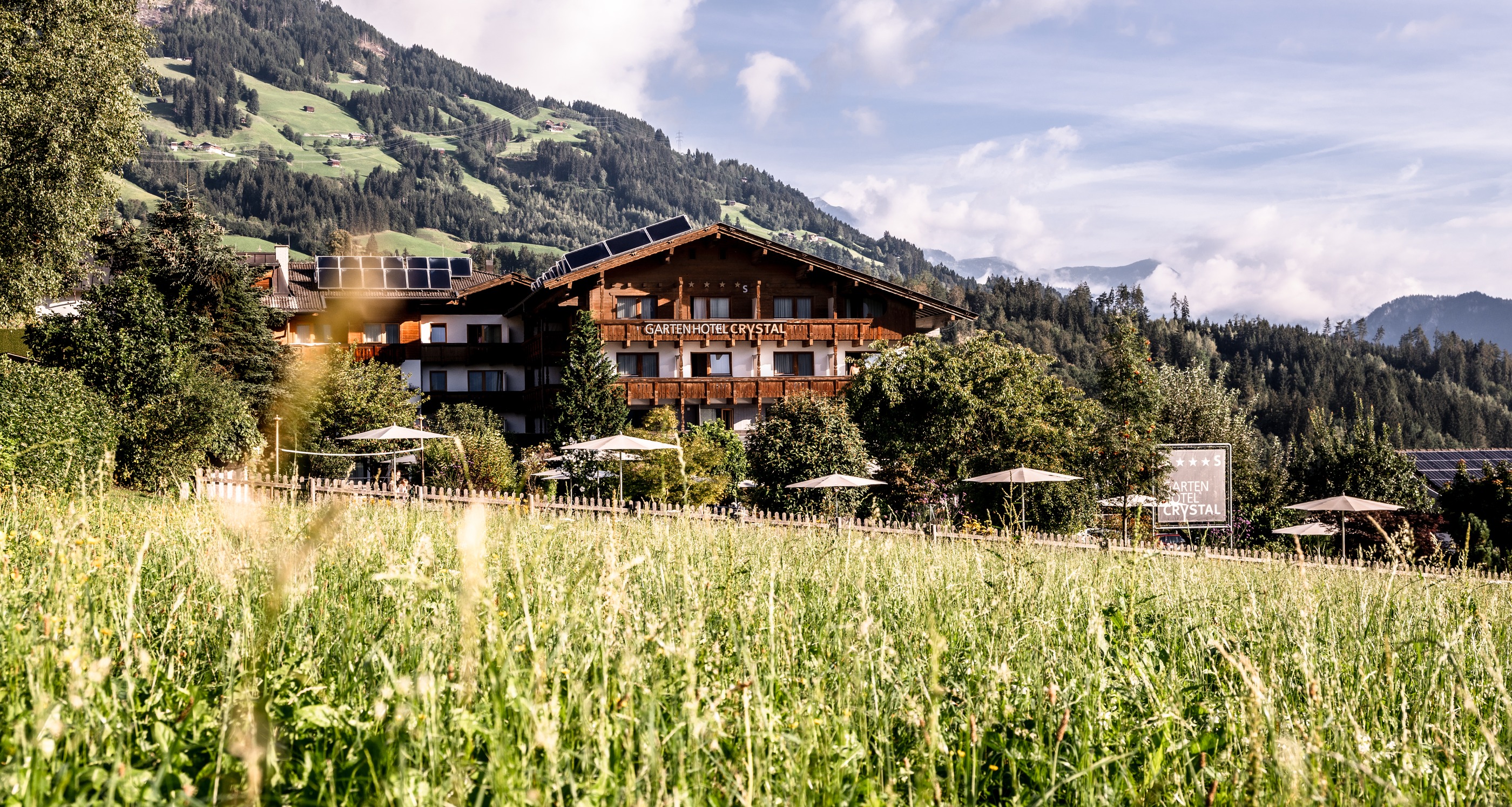 Gardenhotel Crystal in Fügen – Panoramablick auf das Hotel mit Alpenkulisse und blühender Wiese | Wellnesshotel Zillertal