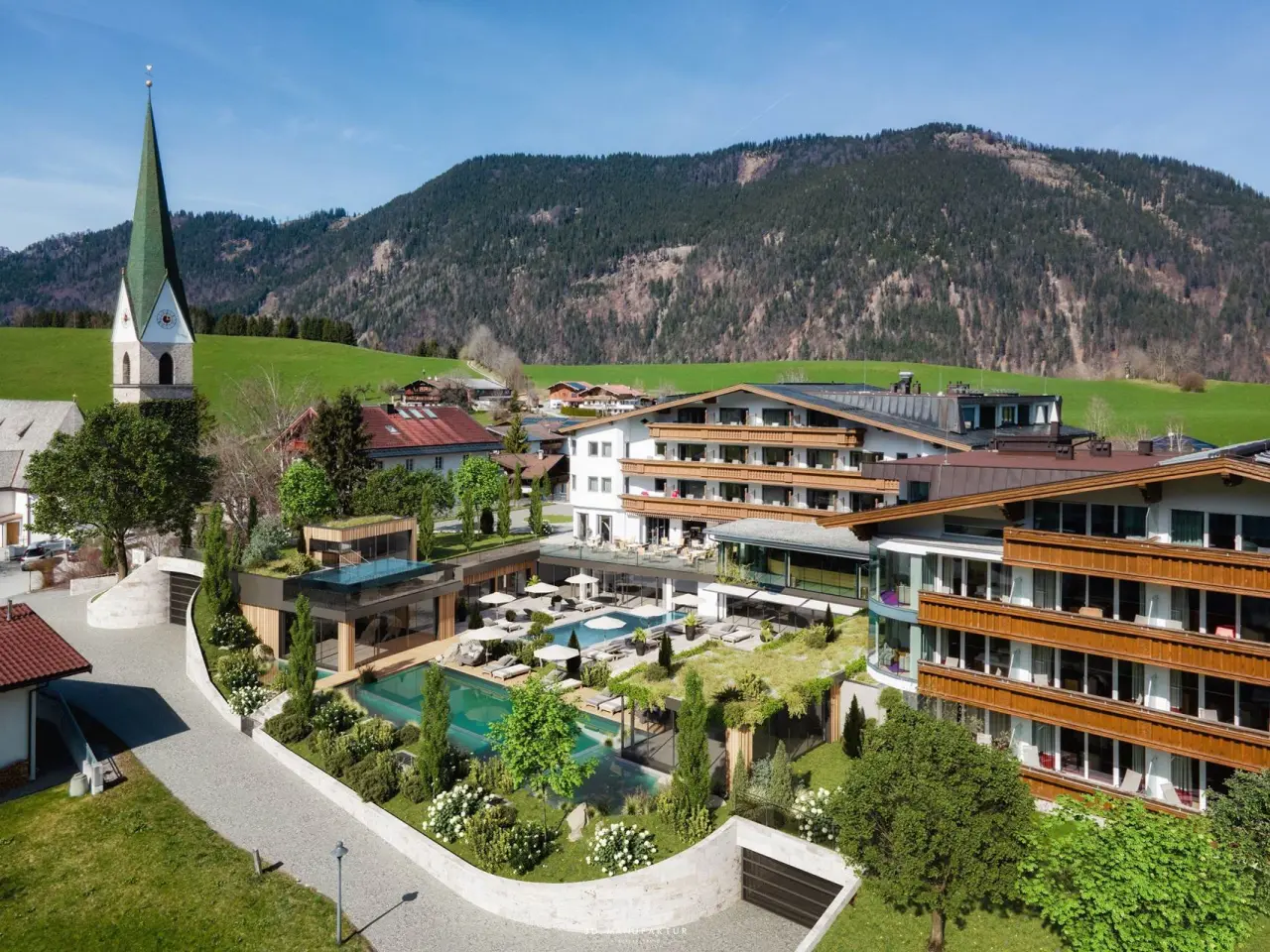 Luftaufnahme des Juffing Hotel & Spa mit Aussenpools, Sonnenterrassen und Bergpanorama in den österreichischen Alpen.