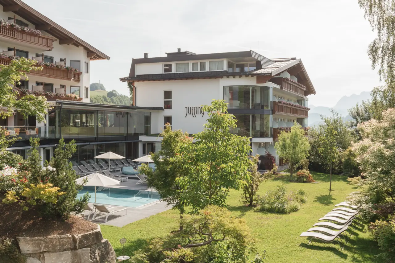 Aussenansicht des Juffing Hotel & Spa mit sonnigem Aussenpool, Liegewiese und Alpenpanorama im Hintergrund.