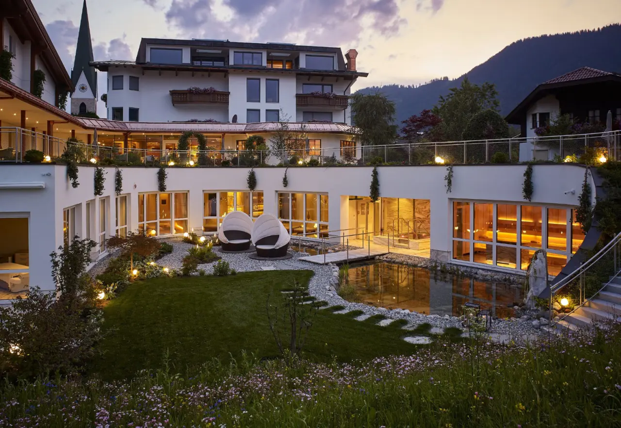 Abendliche Aussenansicht des Juffing Hotel & Spa mit beleuchtetem Wellness-Garten, Naturteich und Einblick in den Spa-Bereich.