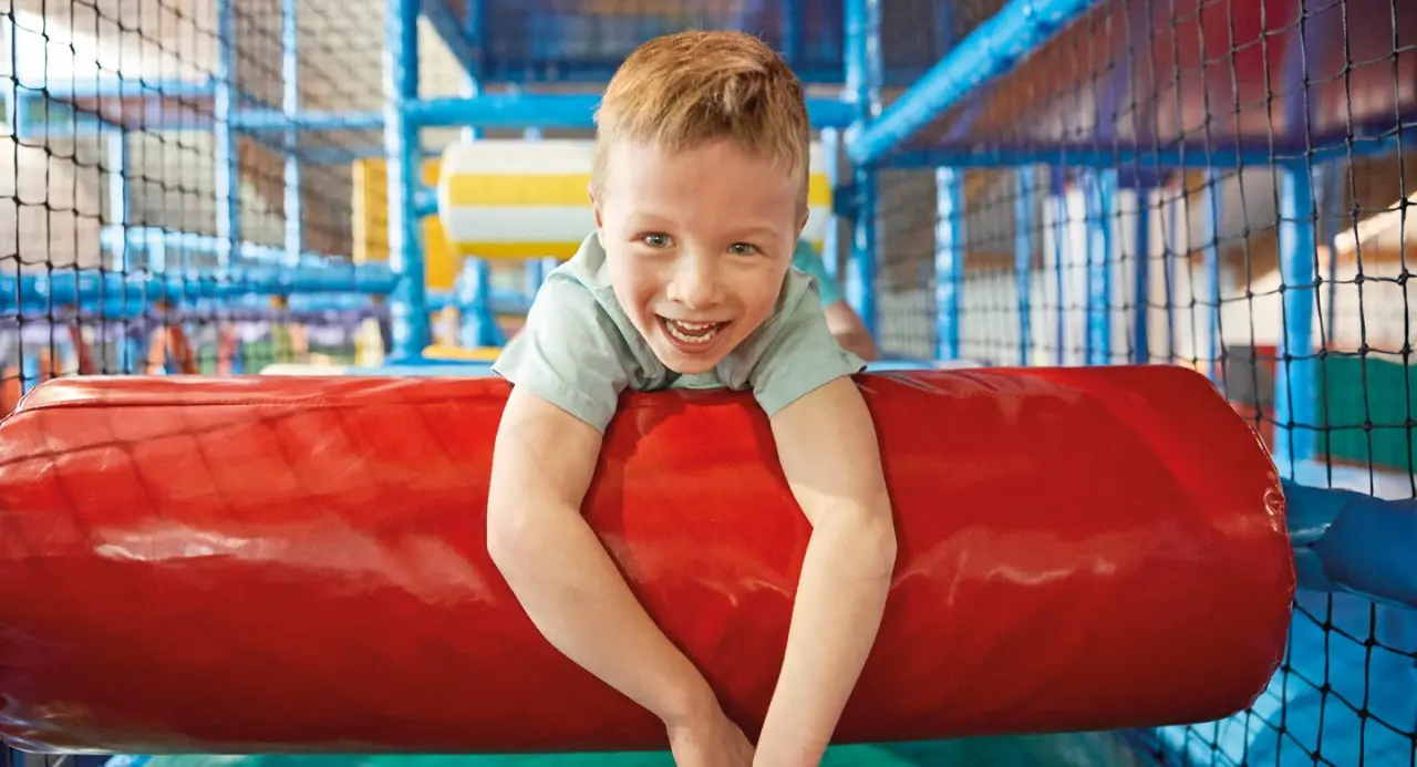 Lachendes Kind im bunten Indoor-Spielplatz des Aldiana Club Ampflwang, ideal für Familienurlaub.