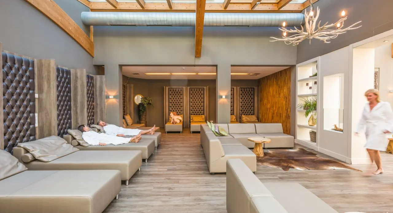 Grosszügiger Ruheraum im Spa des Aldiana Club Ampflwang mit bequemen Liegen, Tageslicht und entspannten Gästen in Bademänteln.