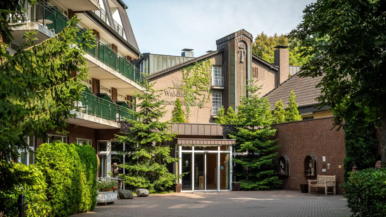 Aussenansicht des Waldhotel Tannenhäuschen mit grüner Fassade, Balkonen und einladendem Eingangsbereich unter blauem Himmel.