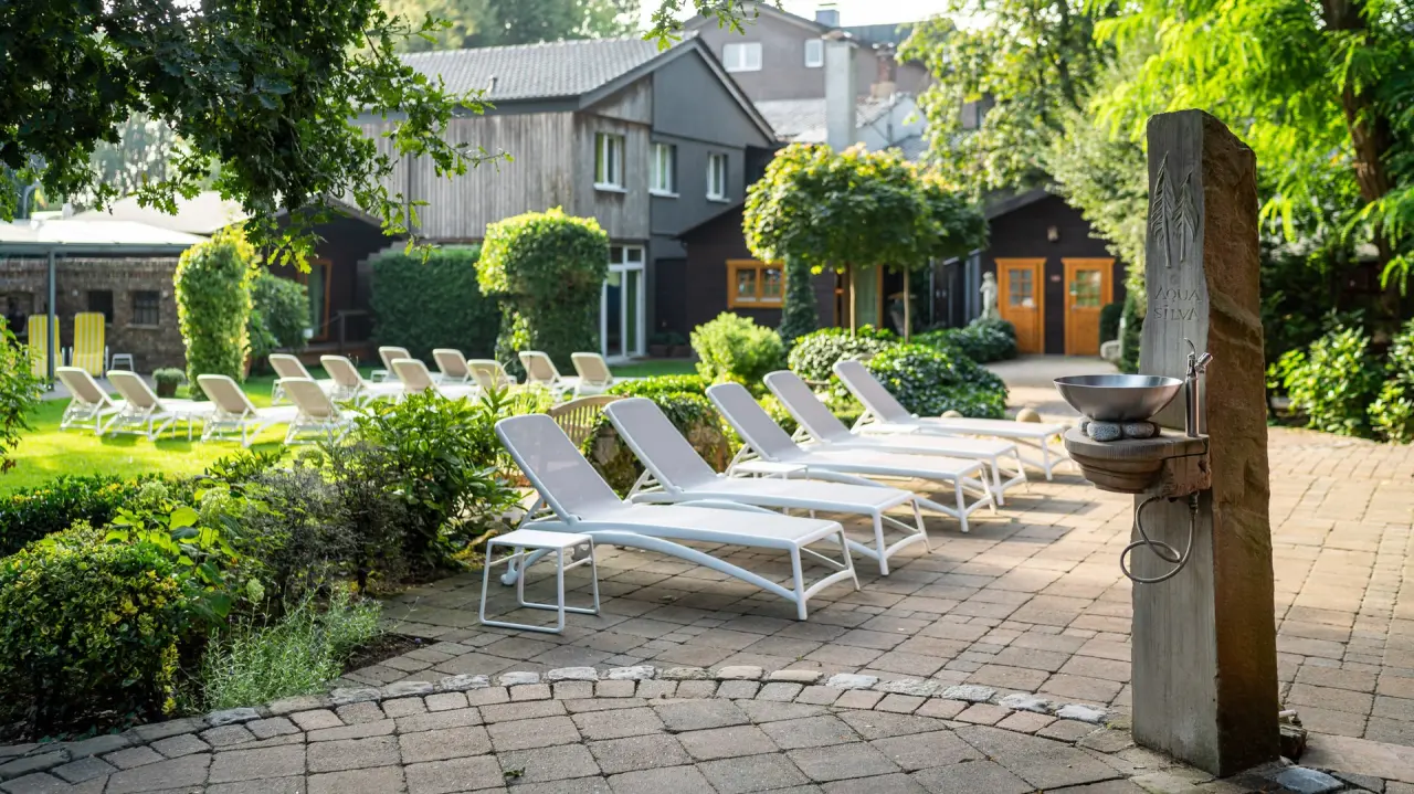 Sonnige Liegewiese mit bequemen Liegestühlen und Naturstein-Trinkbrunnen im Garten des Waldhotel Tannenhäuschen.
