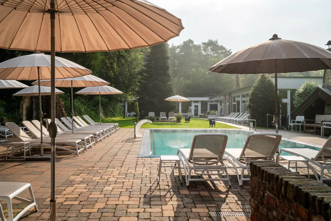 Aussenpool mit Liegestühlen und Sonnenschirmen im grünen Garten des Waldhotel Tannenhäuschen an einem sonnigen Tag.