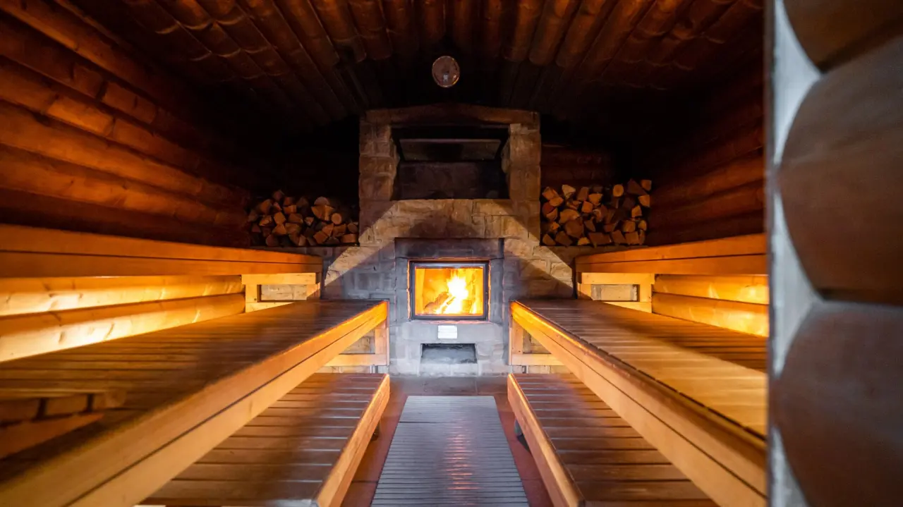 Gemütliche Holzsauna mit knisterndem Kaminfeuer und bequemen Bänken im Waldhotel Tannenhäuschen.