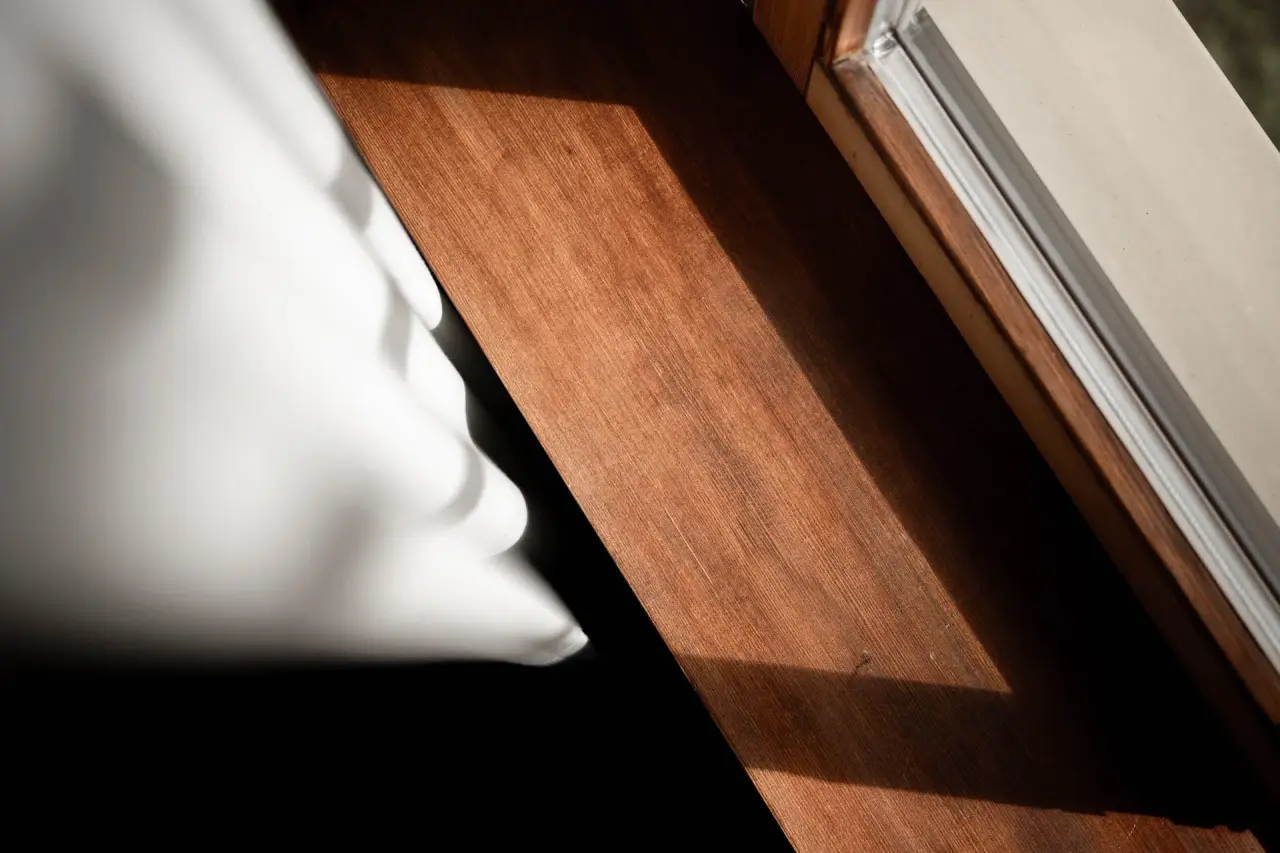 Detailaufnahme eines Holzfensterbretts mit weissem Vorhang und Sonnenlicht im A-ROSA Kitzbühel.