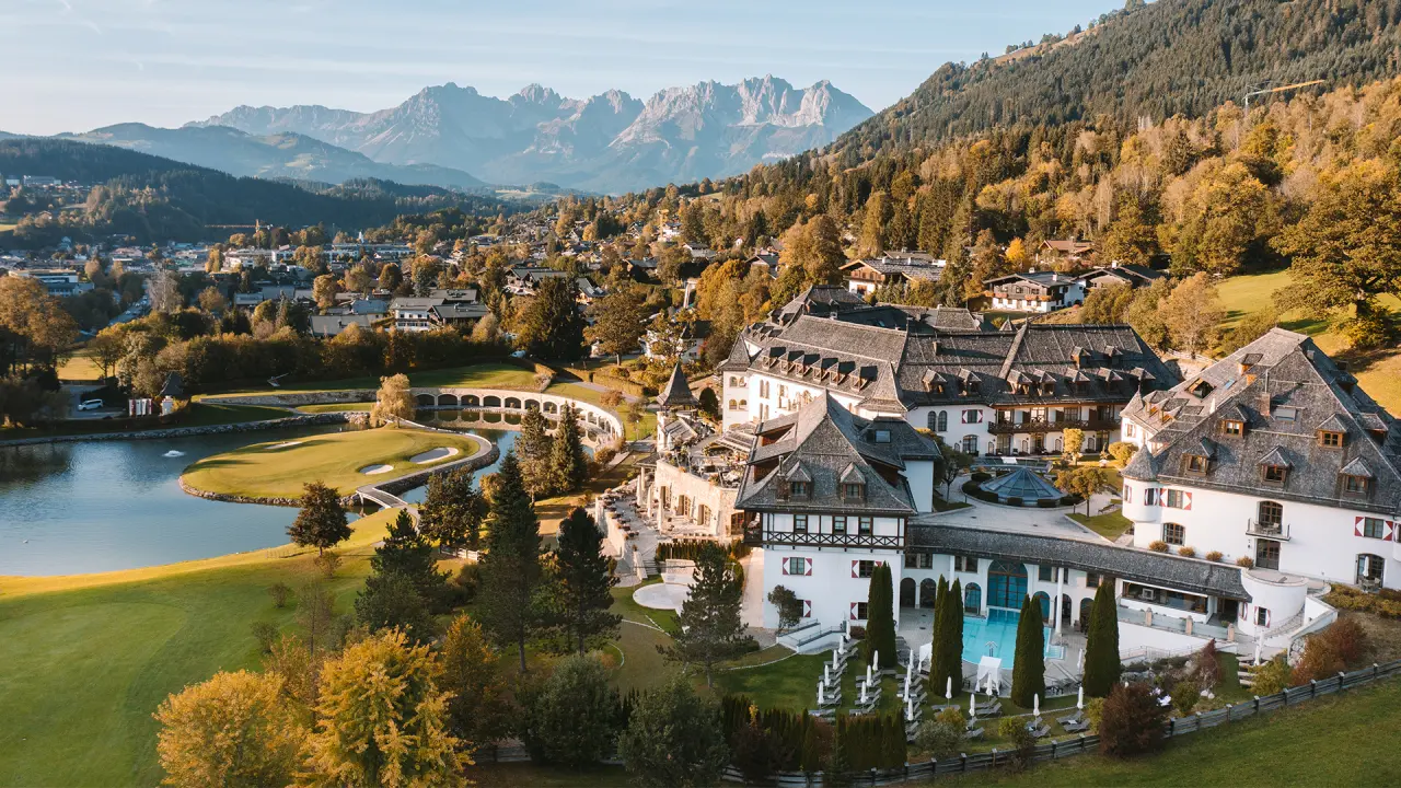 Luftaufnahme des A-ROSA Kitzbühel mit Hotelanlage, Outdoor-Pool, Golfplatz und majestätischem Bergpanorama.