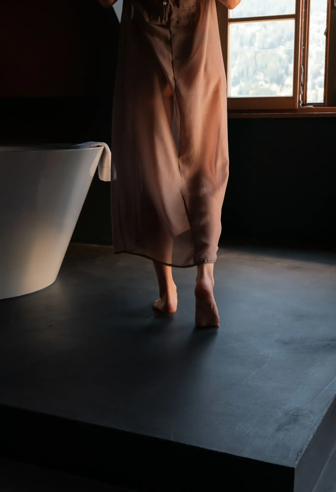 Person im Bademantel vor freistehender Badewanne mit Ausblick im A-ROSA Kitzbühel.