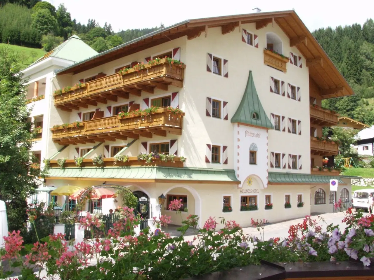 Aussenansicht des traditionellen Wellnesshotels Mitterwirt mit blühenden Blumen und Bergkulisse.