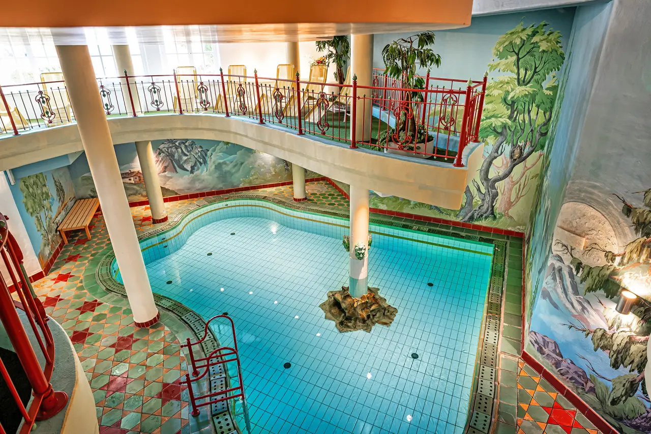 Innenpool im Hotel Mitterwirt mit farbenfrohen Wandmalereien, Galerie und roten Geländern.
