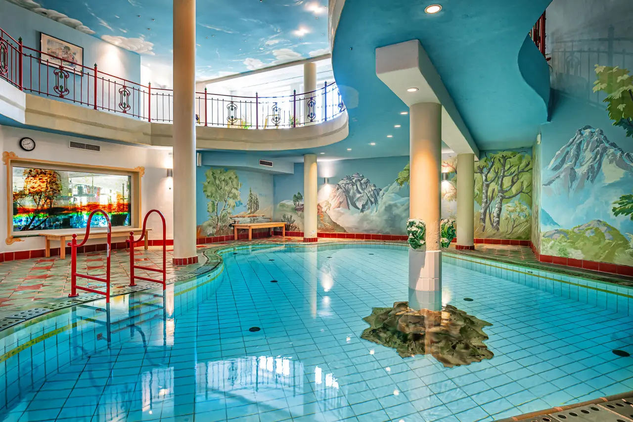 Großzügiger Innenpool mit farbenfrohen Wandmalereien und umlaufender Galerie im Wellnessbereich des Hotel Mitterwirt.