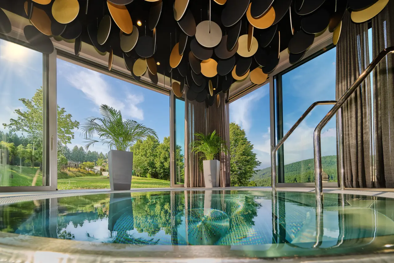 Moderner Indoor-Pool im Hotel Reinerhof mit Design-Decke und Panorama-Blick ins Grüne für entspannende Momente.
