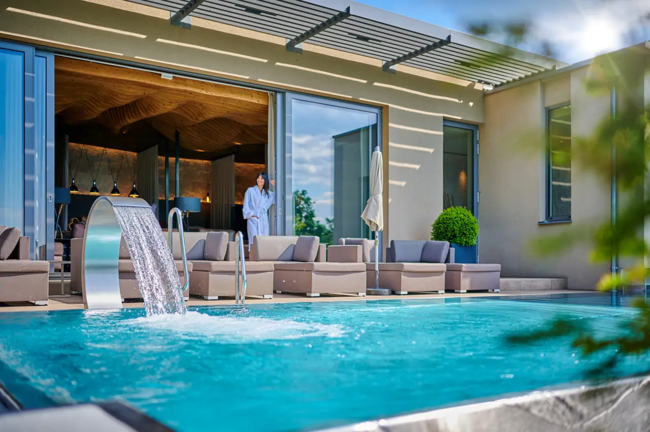 Luxuriöser Aussenpool mit Wasserfall und Lounge-Terrasse im Hotel Reinerhof. Gast im Bademantel genießt den Wellnessbereich.