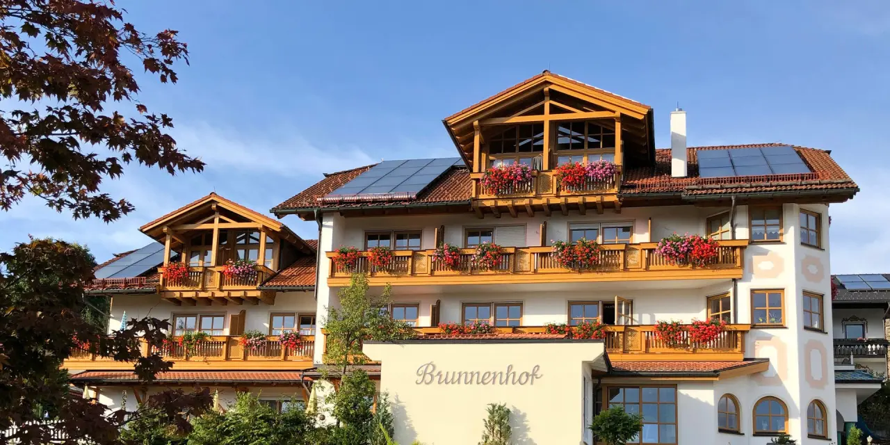 Aussenansicht des Hotel Brunnenhof mit traditioneller Architektur, blumengeschmückten Balkonen und Solaranlagen auf dem Dach.