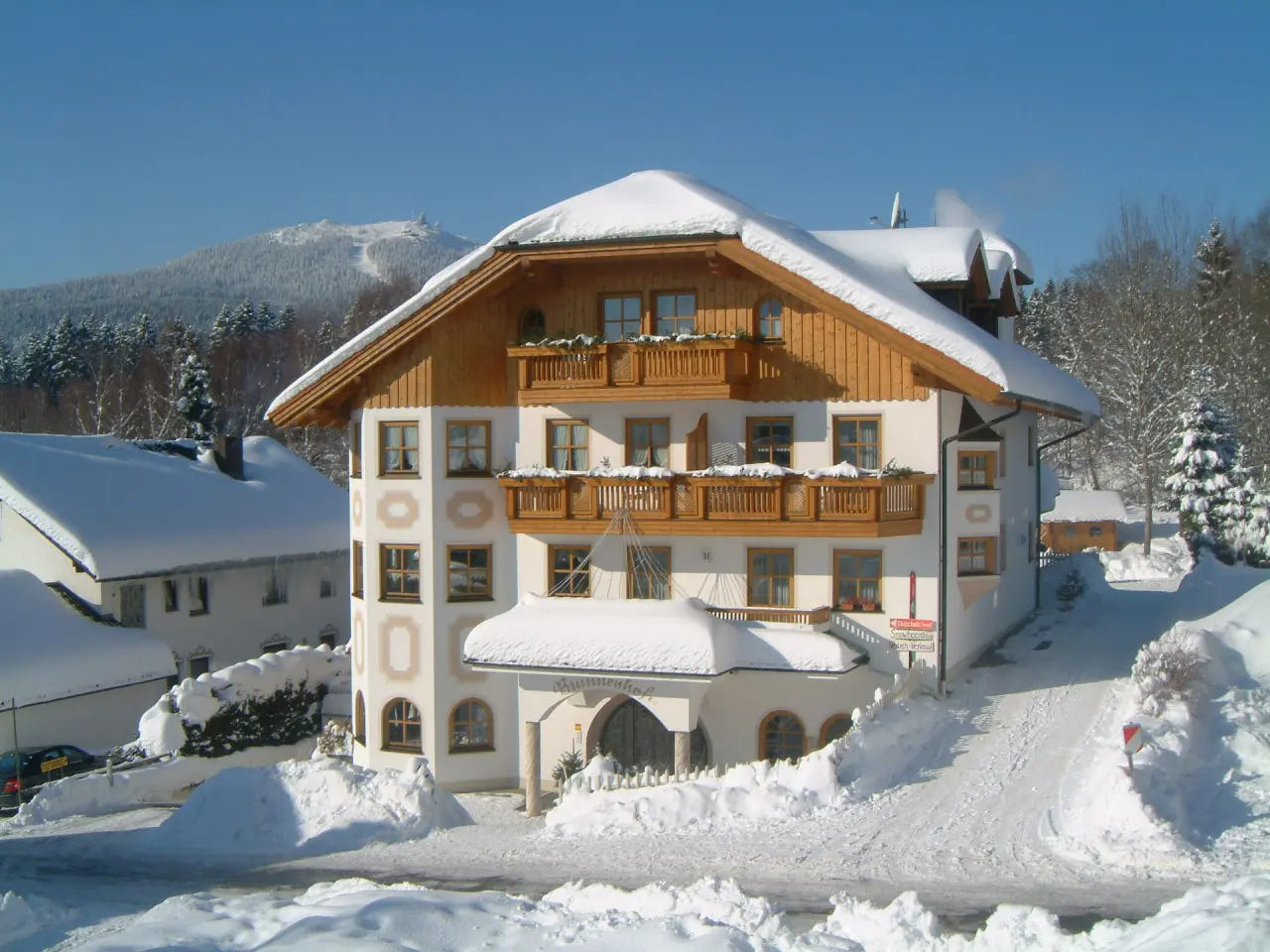 Verschneites Hotel Brunnenhof in den bayerischen Alpen im Winter, mit traditioneller Architektur und blauem Himmel.