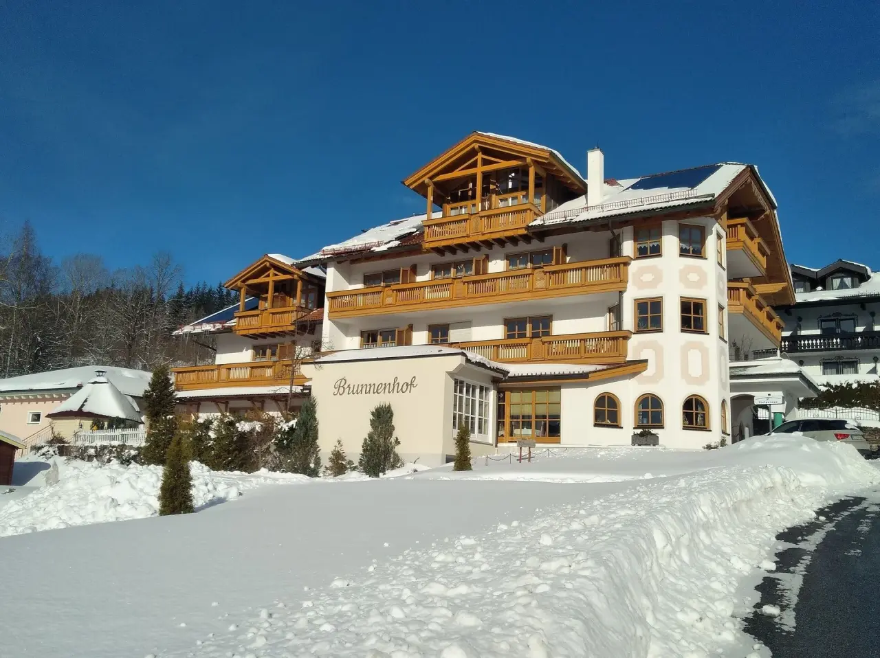 Aussenansicht des Hotel Brunnenhof im Winter mit traditioneller Architektur, verschneiter Landschaft und klarem blauen Himmel.