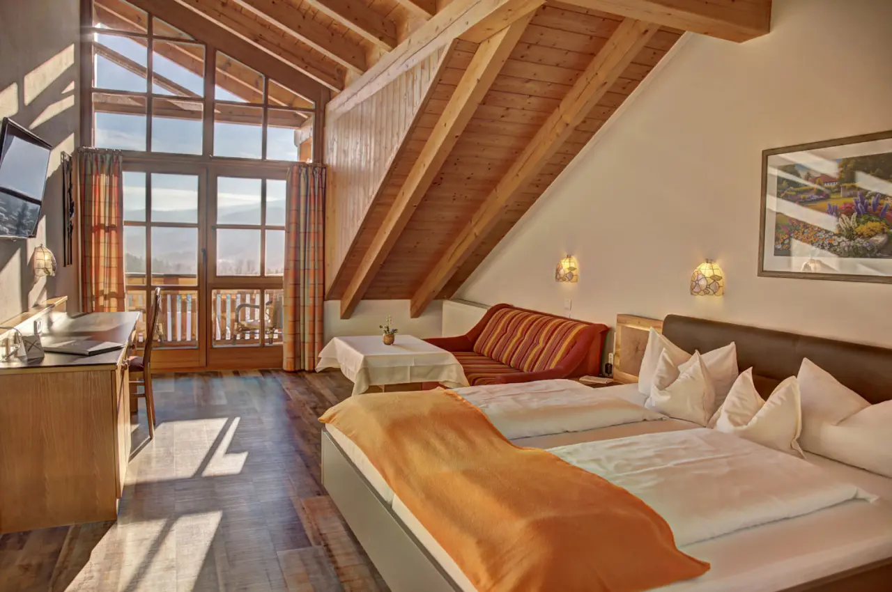 Gemütliches Hotelzimmer im Dachgeschoss des Hotel Brunnenhof mit Holzbalken, Doppelbett, Sitzecke und Bergblick.