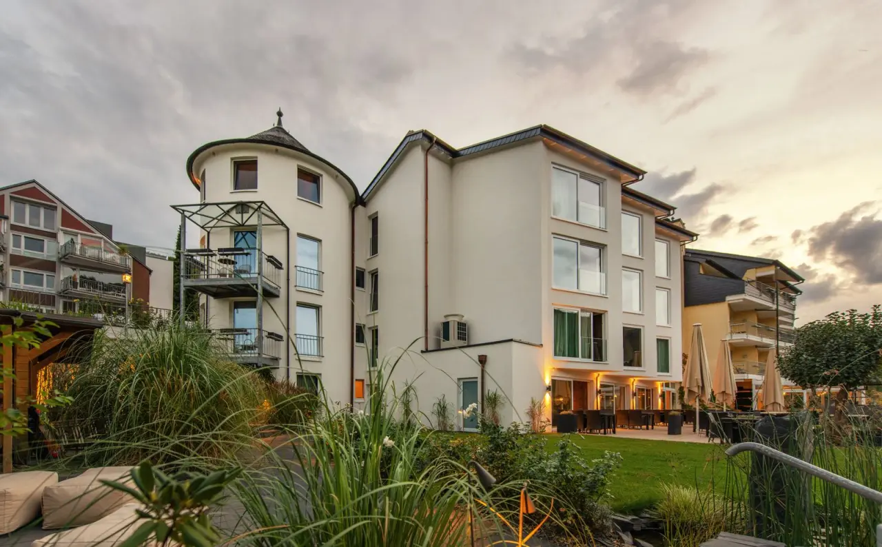 Modernes Moselromantik Hotel Keßler-Meyer bei Dämmerung mit beleuchteter Fassade, Rundturm und einladendem Garten.