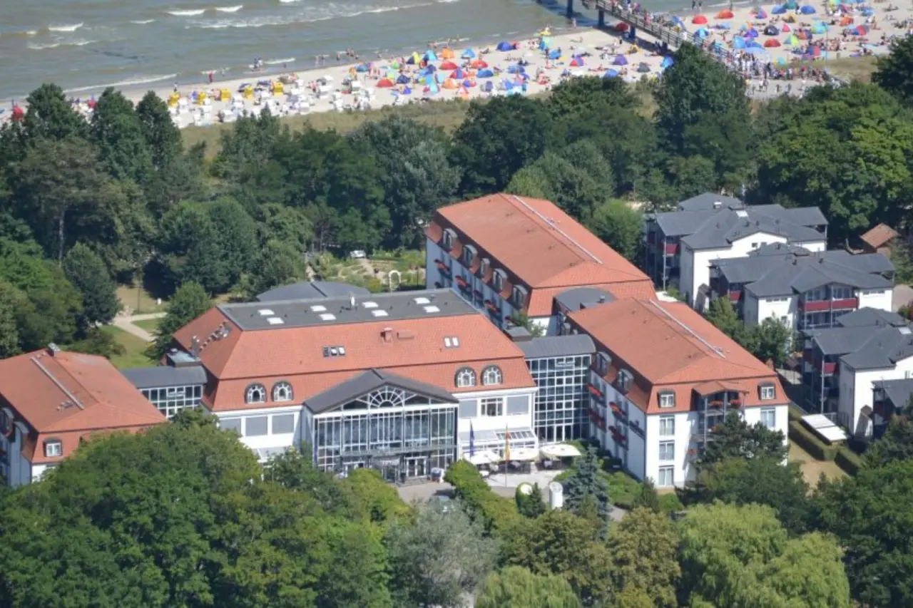 Luftaufnahme des Seehotel Grossherzog v. Mecklenburg mit rotem Dach, umgeben von Gruen, direkt am Strand und der Seebruecke.
