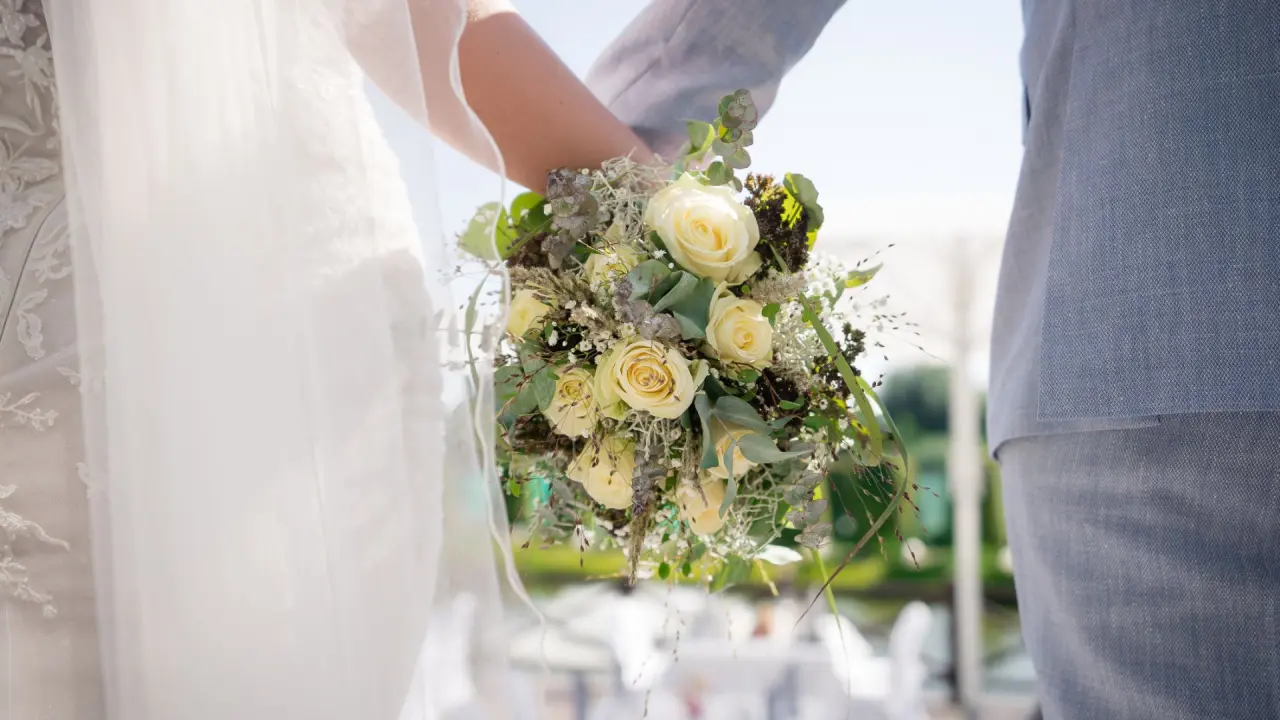 Brautpaar hält Hochzeitsstrauß mit cremefarbenen Rosen und Eukalyptus im COURT HOTEL.