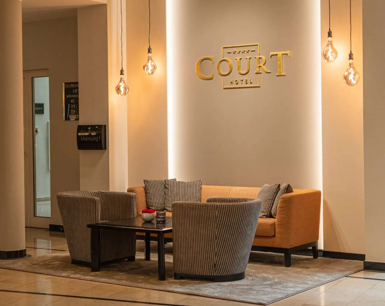 Einladende Lobby des COURT HOTEL mit bequemen Sitzgelegenheiten, stilvoller Beleuchtung und Hotel-Logo.