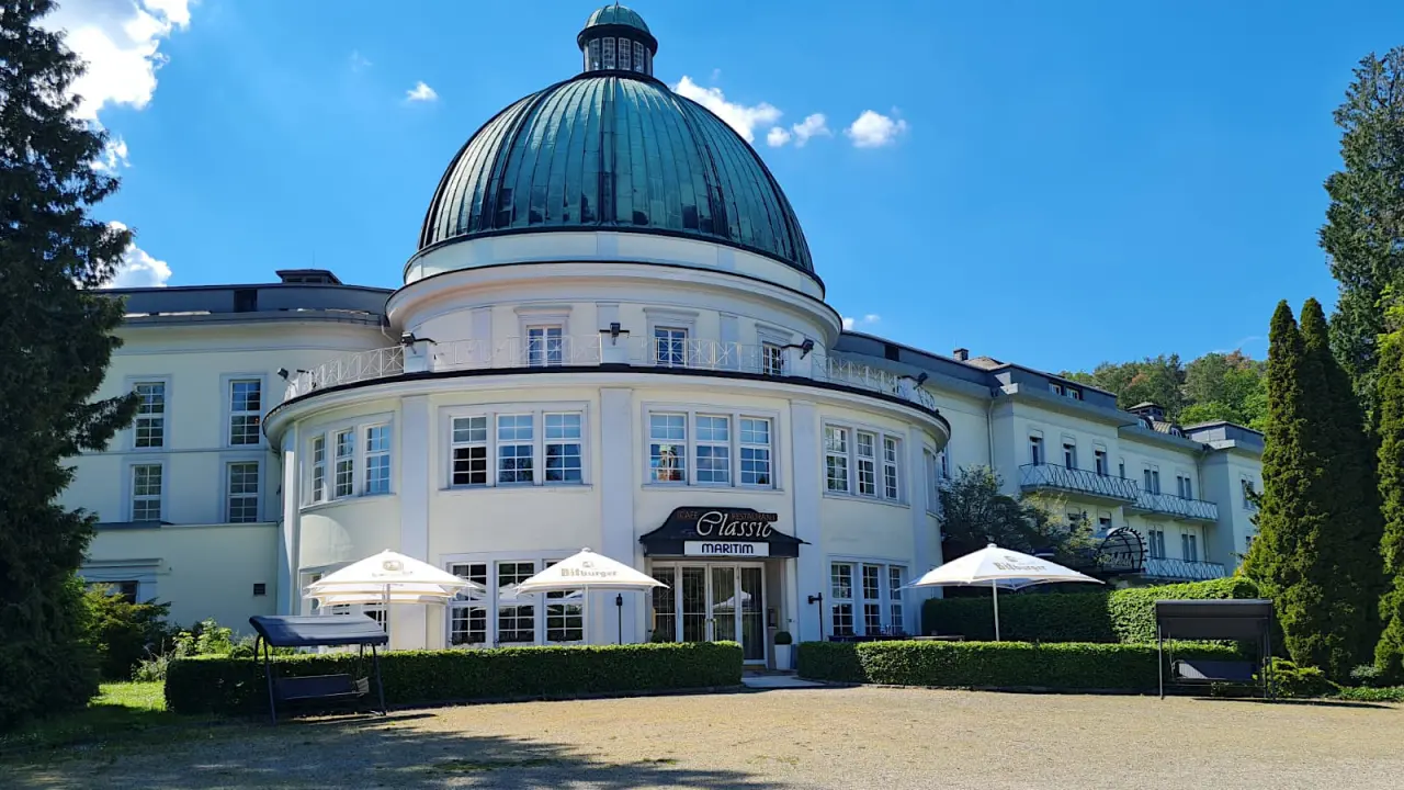 Majestätische Aussenansicht des Maritim Hotel Bad Wildungen mit markanter Kuppel und grüner Umgebung unter blauem Himmel.