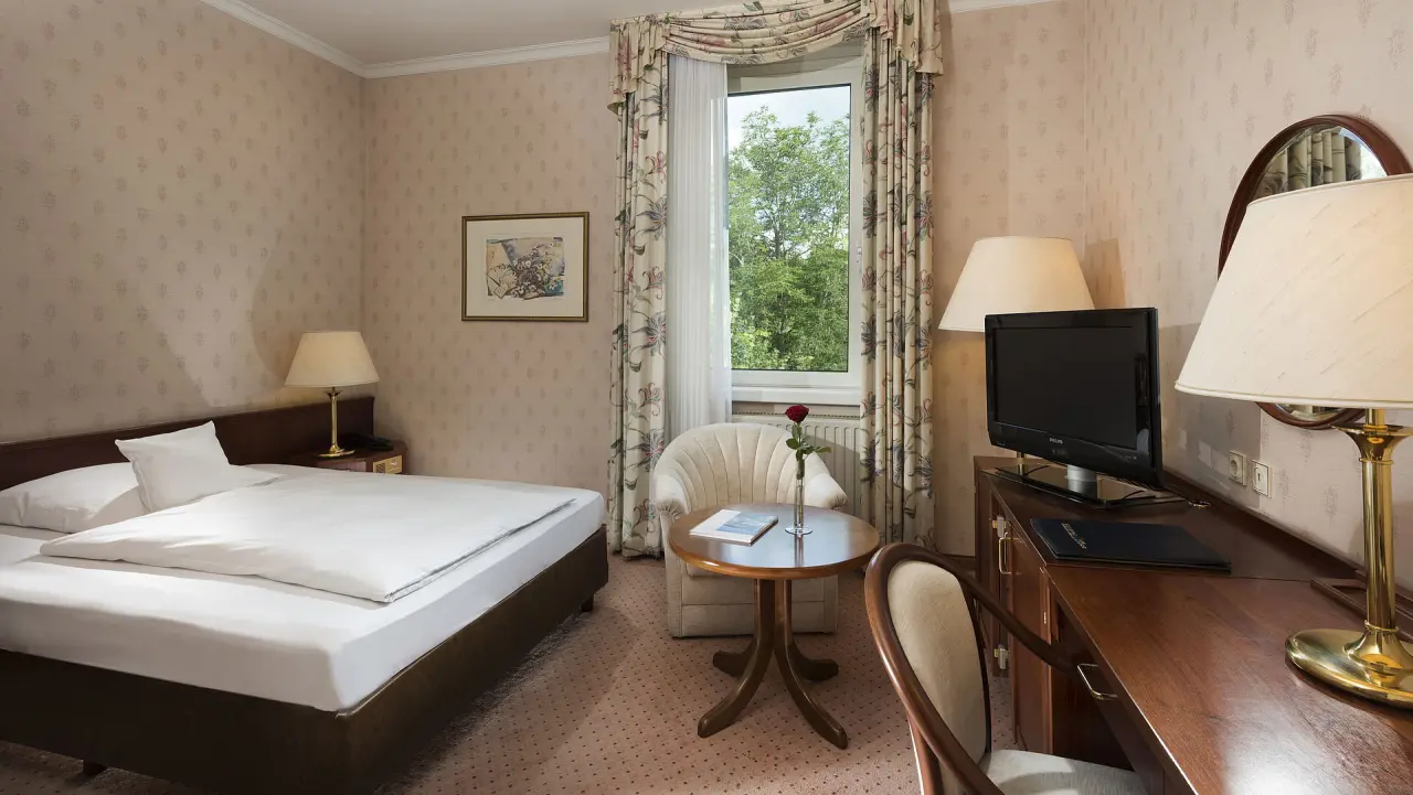 Gemütliches Einzelzimmer mit Bett, Schreibtisch und Blick ins Grüne im Maritim Hotel Bad Wildungen.