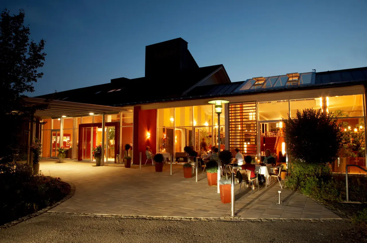 Beleuchtete Aussenansicht des Vitalhotel Vierjahreszeiten bei Nacht mit beleuchteter Terrasse und Gästen.