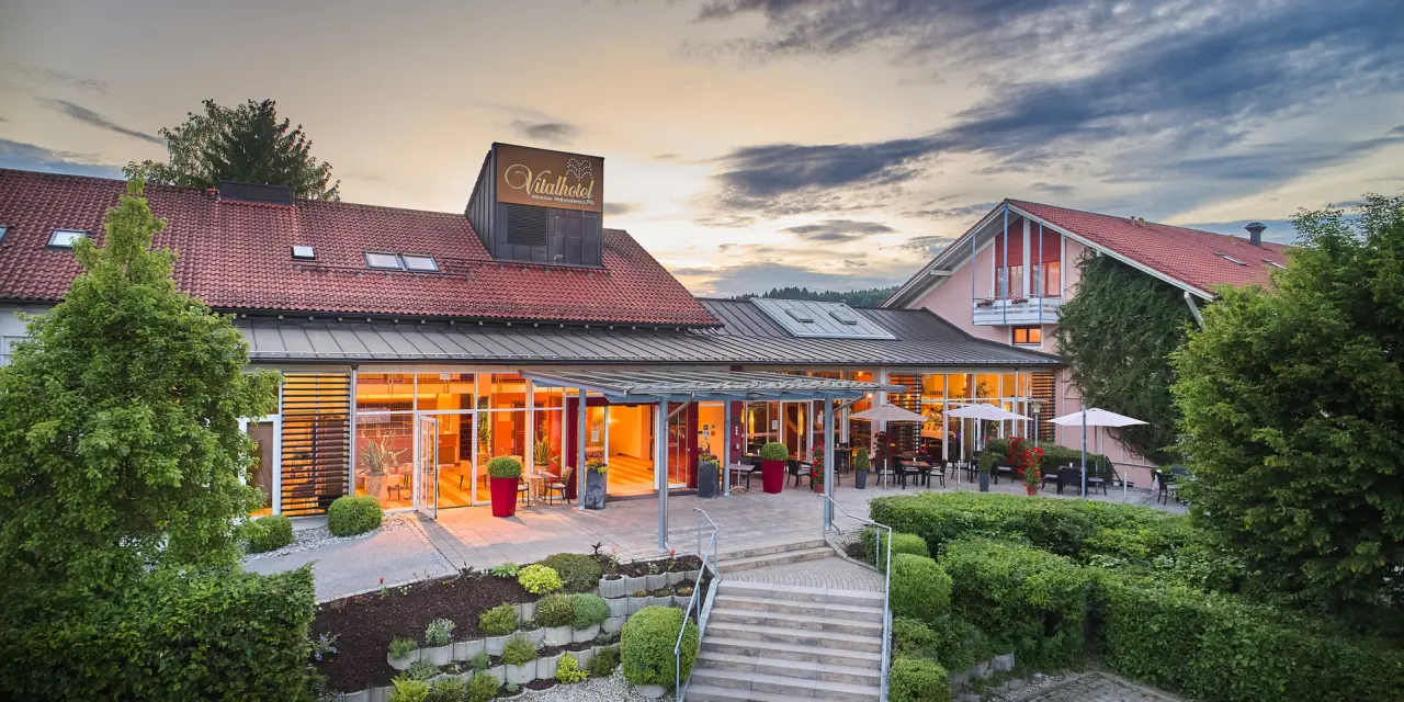 Einladende Aussenansicht des Vitalhotel Vierjahreszeiten bei Sonnenuntergang mit beleuchtetem Eingang und Terrasse.