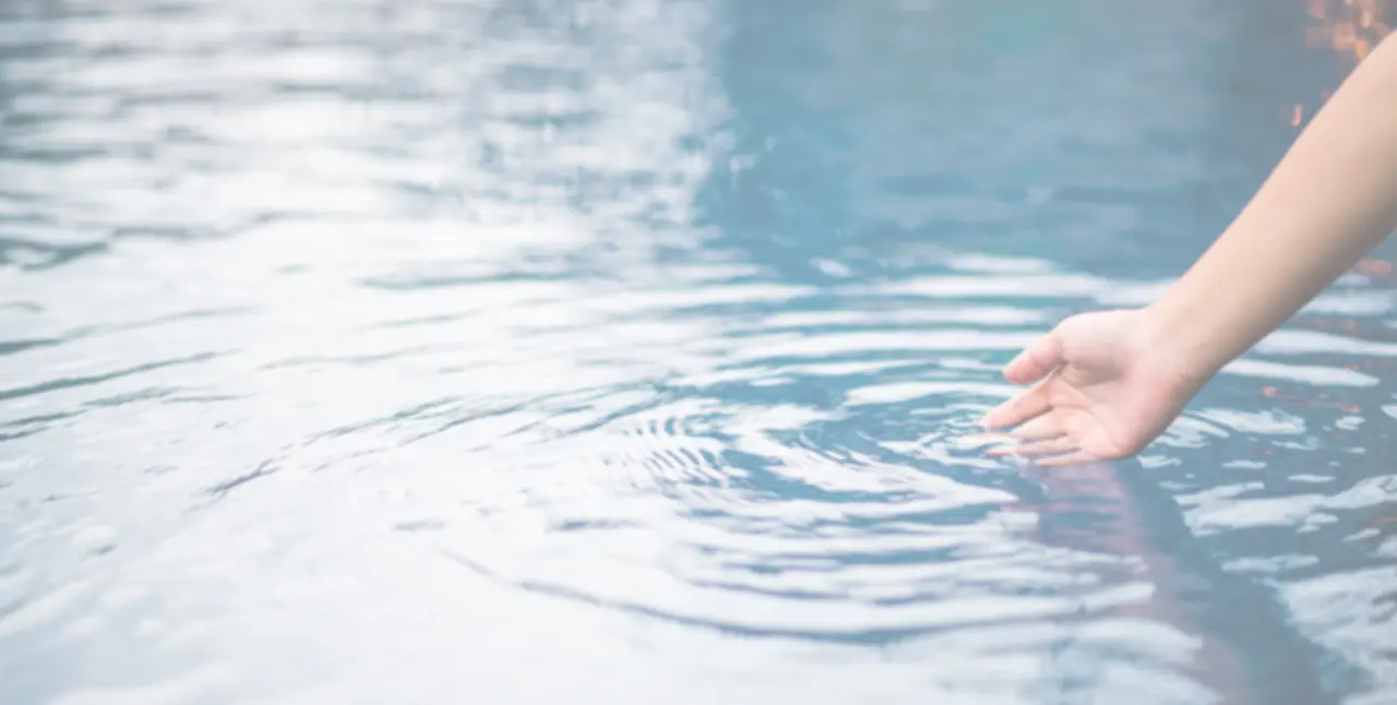 Hand berührt sanft die Wasseroberfläche im Pool des Vitalhotel Vierjahreszeiten.