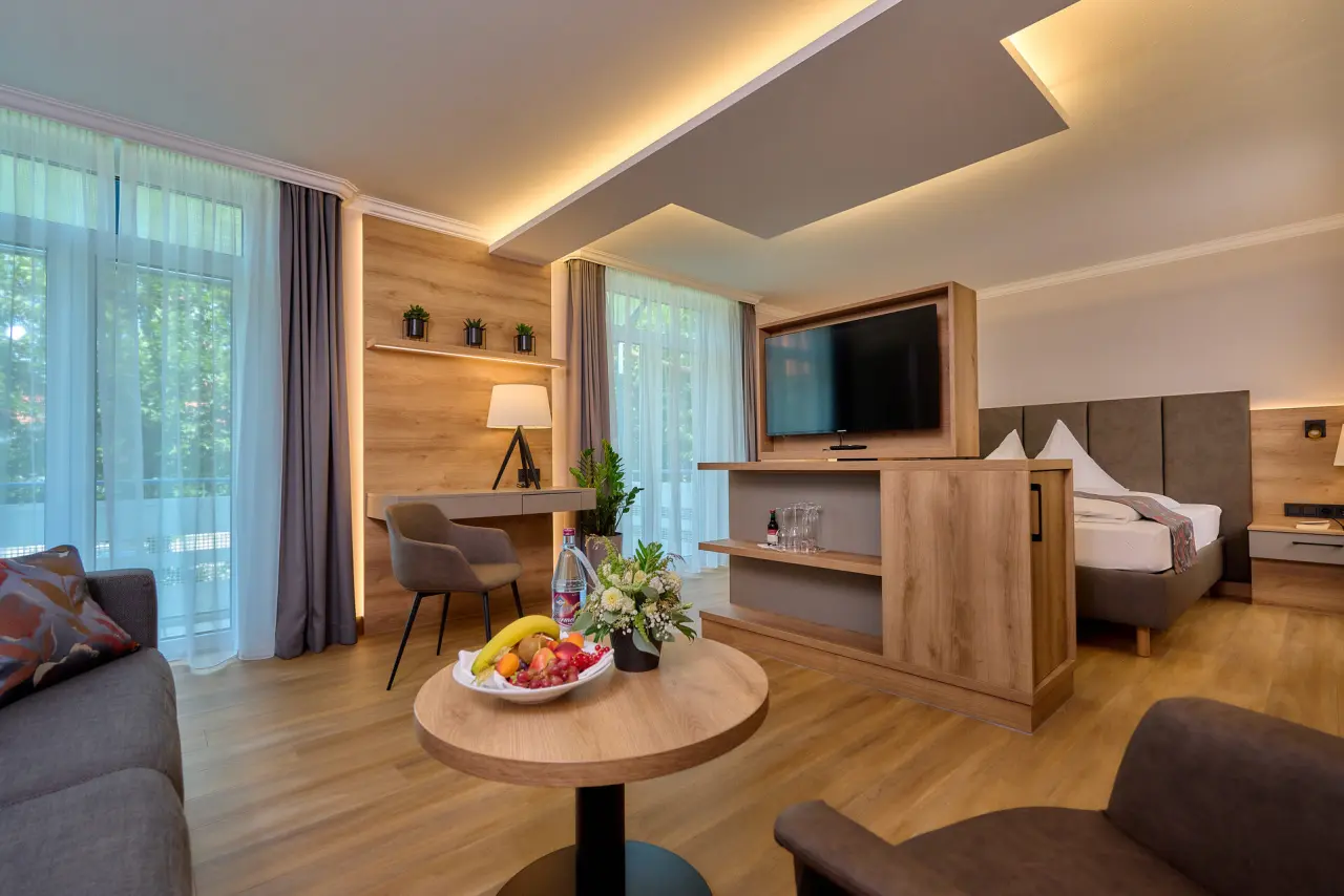 Helle und moderne Suite im Vitalhotel Vierjahreszeiten mit separatem Wohnbereich, Schreibtisch und Doppelbett.