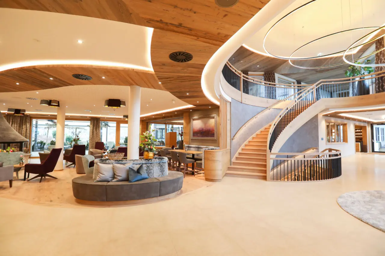 Eindrucksvolle Lobby des Hotel Laschenskyhof mit eleganter Holztreppe, modernen Leuchten und gemuetlichen Sitzbereichen.
