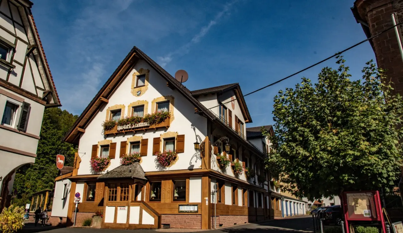 Traditionelles Fachwerk-Hotel Lamm mit Blumenkästen unter blauem Himmel in einer malerischen Gasse.