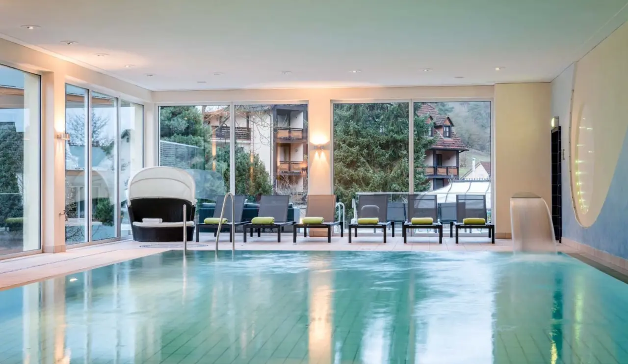 Grosszügiger Innenpool mit Entspannungsliegen und Blick ins Grüne im Wellnessbereich des Hotel Lamm.