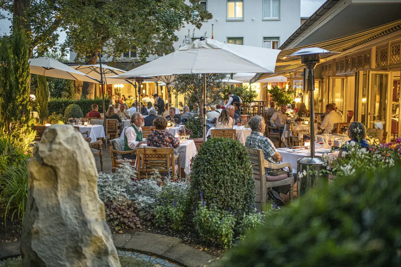 Abendliche Gartenterrasse des Hotel Erbprinz mit Gästen, die unter beleuchteten Sonnenschirmen speisen.