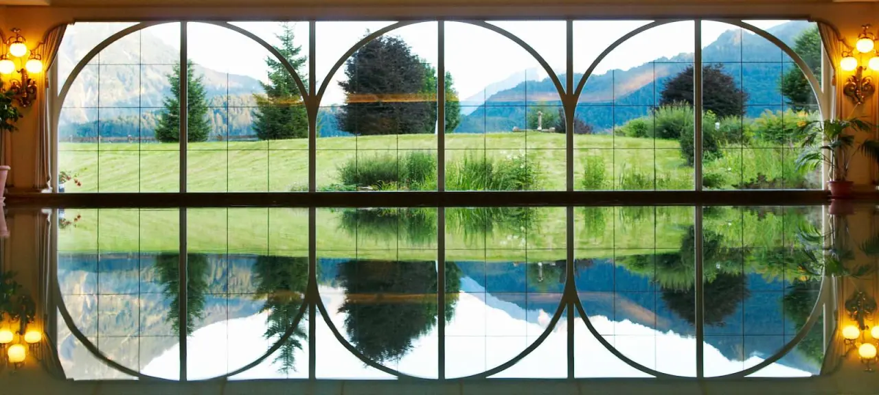 Panoramablick aus dem Innenpool des SCHÜLE'S Gesundheitsresort & Spa auf die Allgäuer Alpen und grüne Wiesen.
