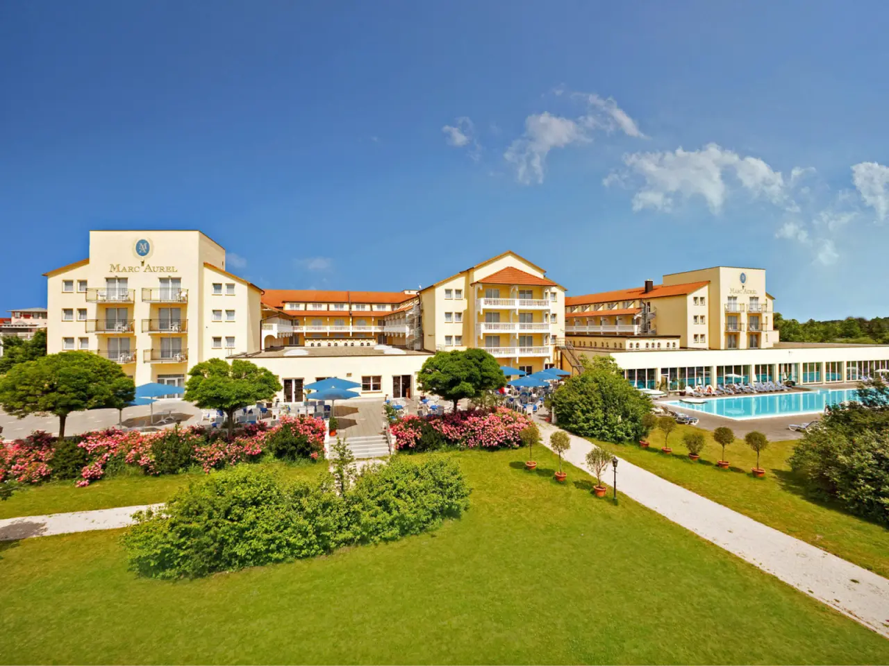 Weitläufige Aussenansicht des Dorint MARC AUREL Resort Bad Gögging mit grosser Poolanlage und gepflegtem Garten unter blauem Himmel.