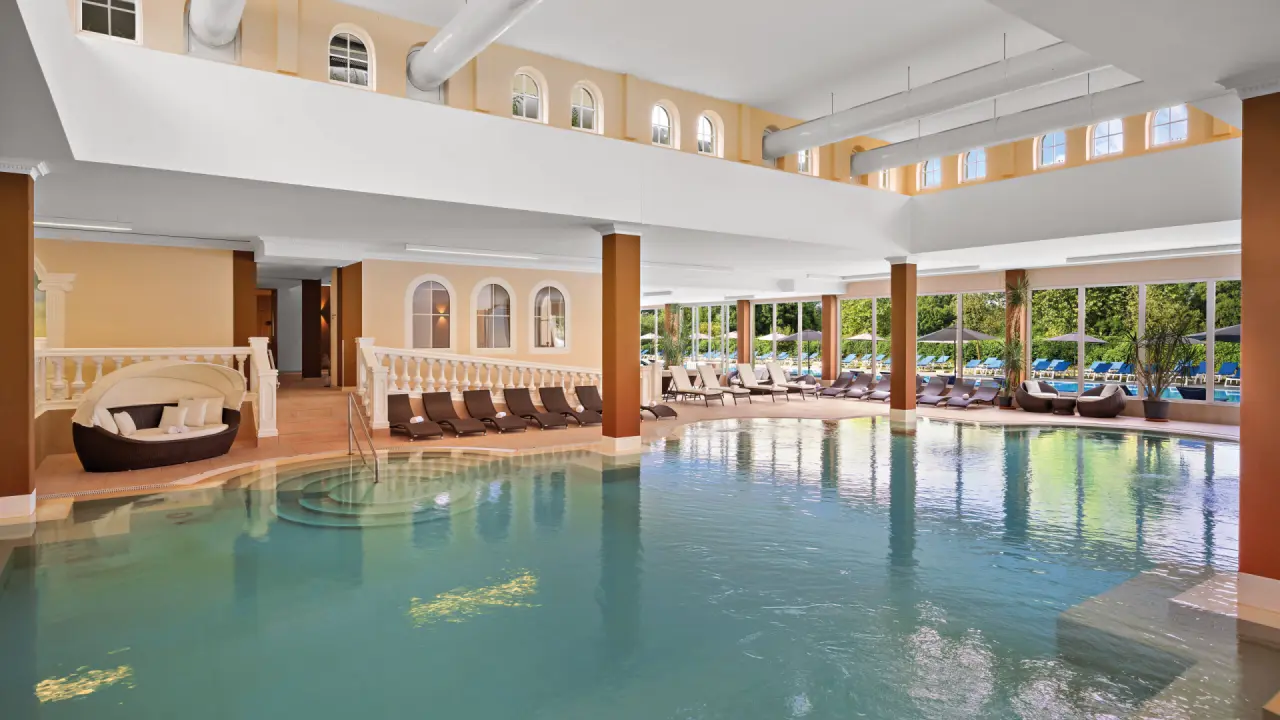 Grosszügiger Innenpoolbereich mit Entspannungsliegen und Blick ins Grüne im Dorint MARC AUREL Resort Bad Gögging