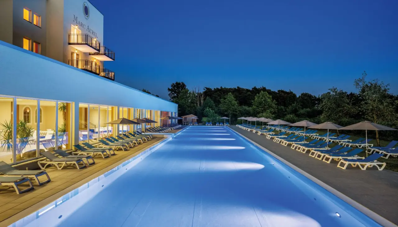Beleuchteter Aussenpool des Dorint MARC AUREL Resort Bad Gögging bei Nacht mit Liegestühlen und Hotelgebäude.