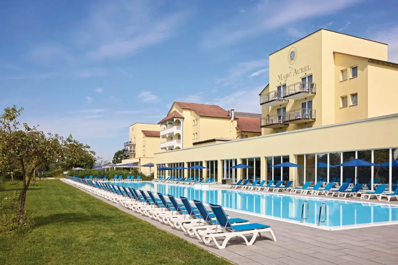 Grosser Aussenpool mit Liegen und dem Hotel Dorint MARC AUREL Resort Bad Gögging unter blauem Himmel.