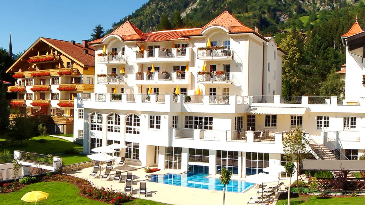 Das Verwöhnhotel Bismarck von aussen mit Pool, Liegewiese und Alpenpanorama an einem sonnigen Tag.