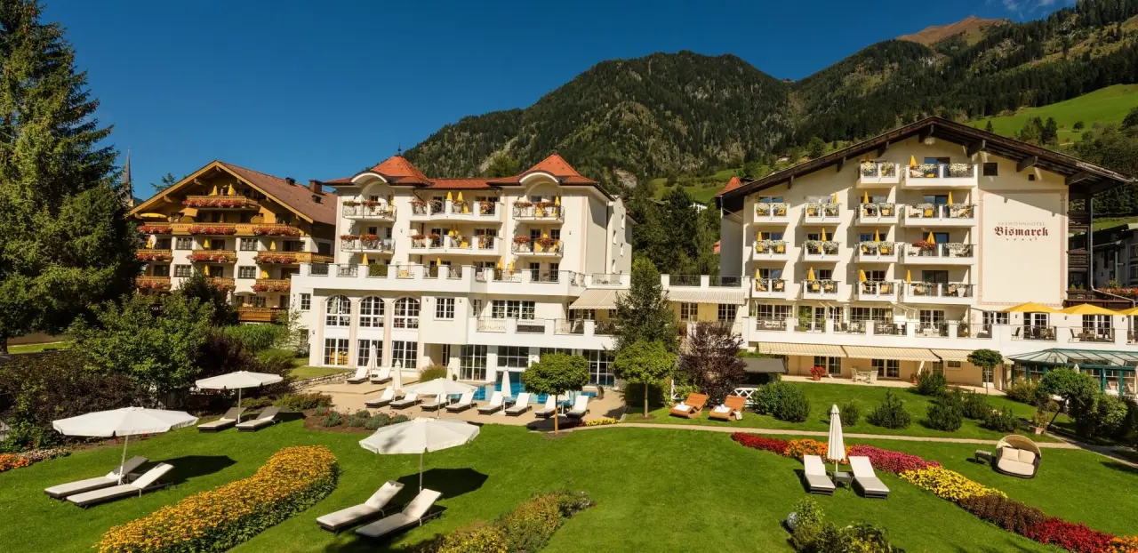 Aussenansicht des Verwöhnhotel Bismarck mit Pool, Liegewiese und Bergpanorama an einem sonnigen Tag.