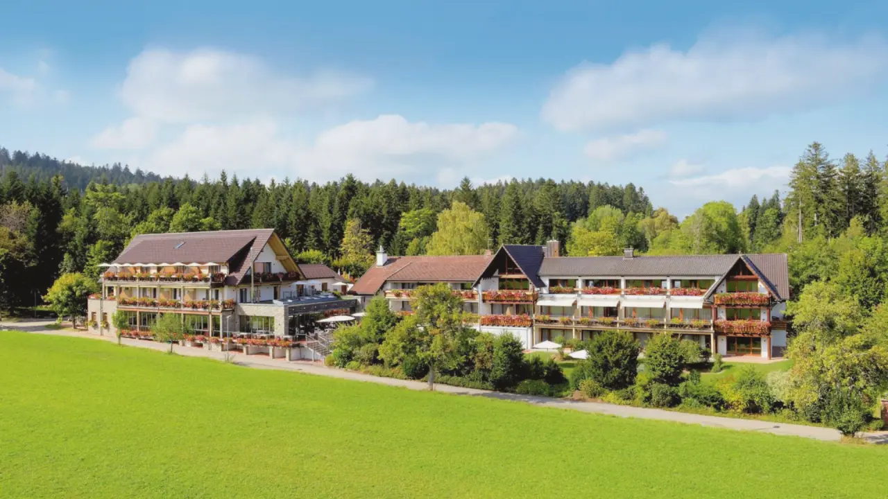 Aussenansicht des Hotel Grüner Wald****S inmitten grüner Wiesen und Wälder unter blauem Himmel.