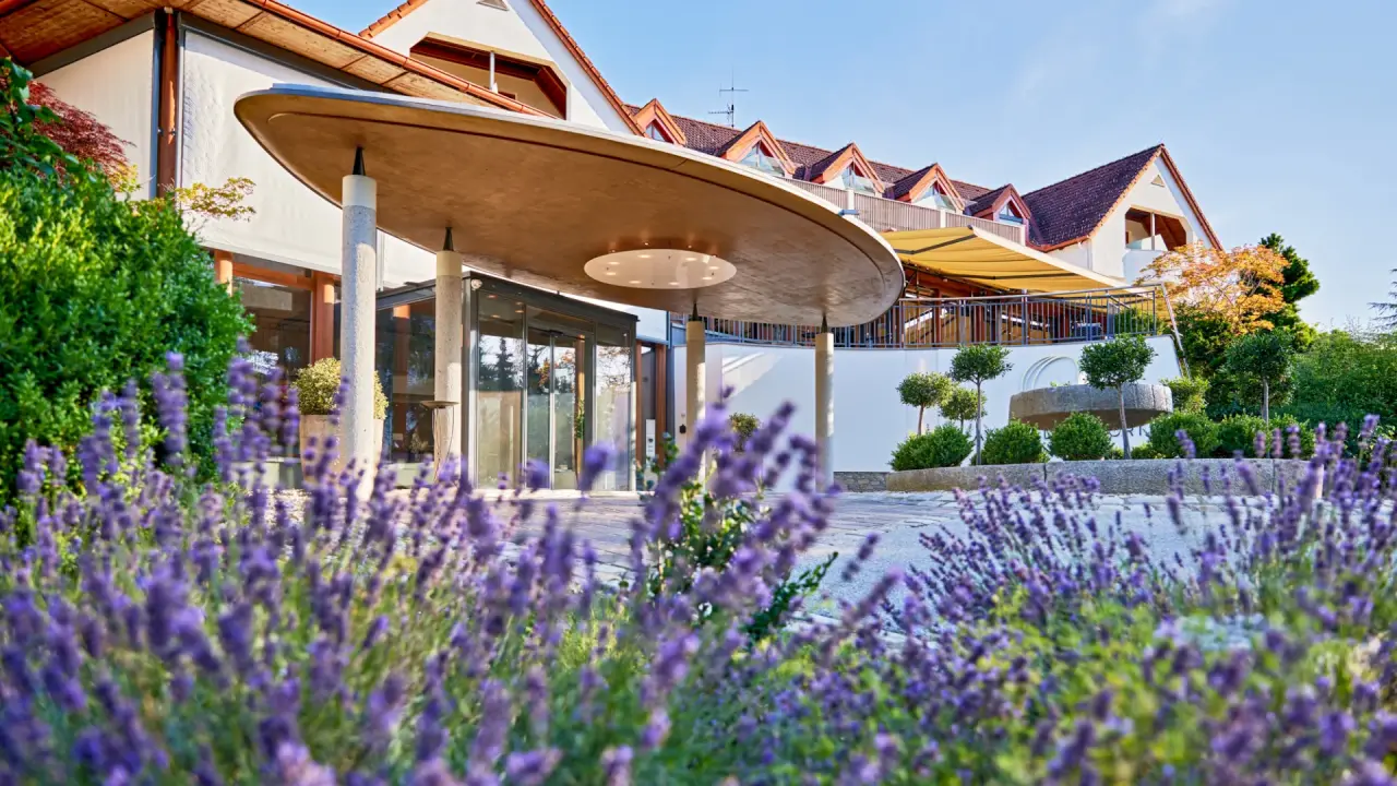 Einladender Haupteingang des Ayurveda Resort Mandira mit moderner Architektur und blühendem Lavendel unter blauem Himmel.