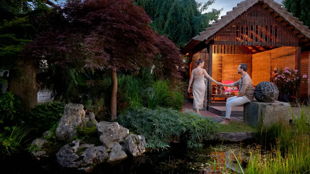 Romantischer Abend im asiatischen Gartenpavillon des Ayurveda Resort Mandira mit entspanntem Paar am Teich.