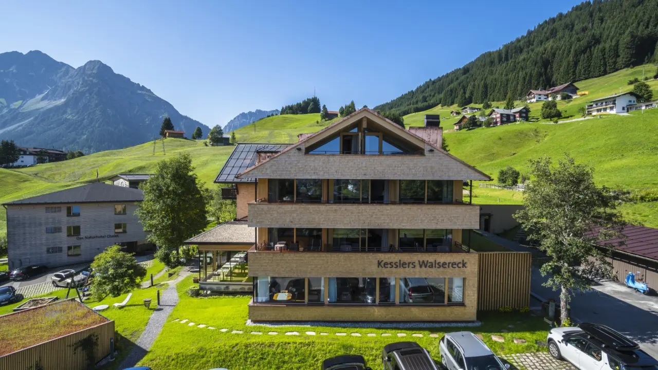 Aussenansicht des Naturhotel Chesa Valisa****s mit traditioneller Architektur, umgeben von grünen Wiesen und majestätischen Bergen.
