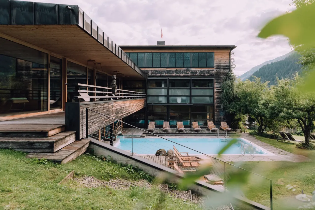 Aussenansicht des Naturhotel Chesa Valisa****s mit grossem Pool, moderner Holzarchitektur und Bergpanorama.