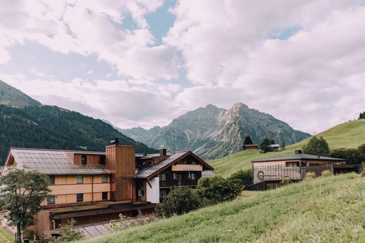 Das Naturhotel Chesa Valisa in den österreichischen Alpen, umgeben von grünen Wiesen und majestätischen Bergen.