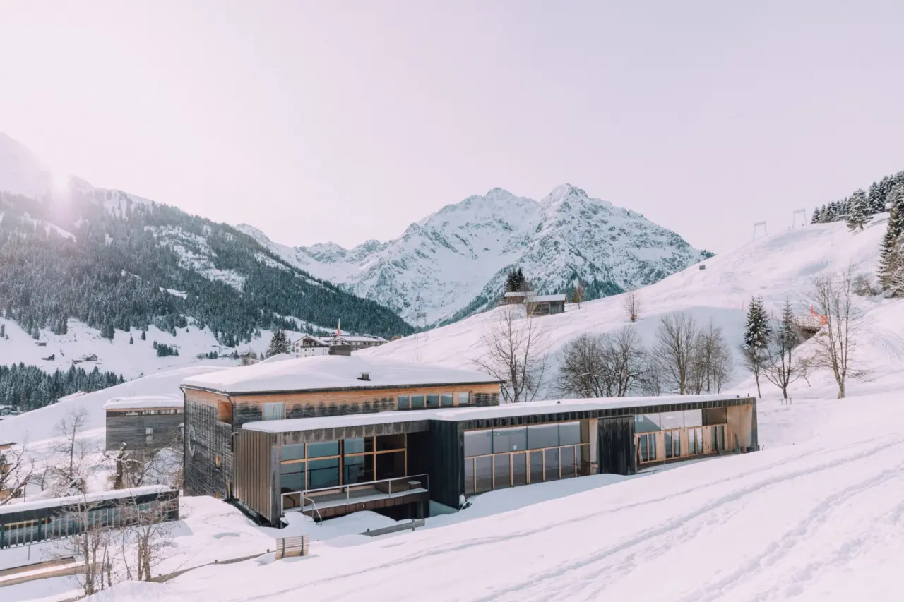 Naturhotel Chesa Valisa im Winter: Modernes Holzhotel umgeben von verschneiten Alpen und Pisten in Vorarlberg.